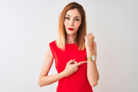 Redhead businesswoman wearing elegant red dress standing over isolated white background In hurry pointing to watch time, impatience, looking at the camera with relaxed expression