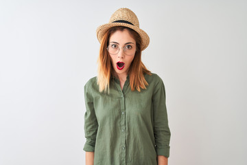 Redhead woman wearing green shirt glasses and hat over isolated white background afraid and shocked with surprise expression, fear and excited face.