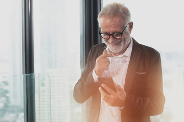 Old Business man smiling while reading a message on his smartphone. Successful business project concept