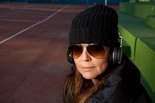 A beautiful woman wearing a black jacket cap a skateboard in the skatepark outdoors and headphones