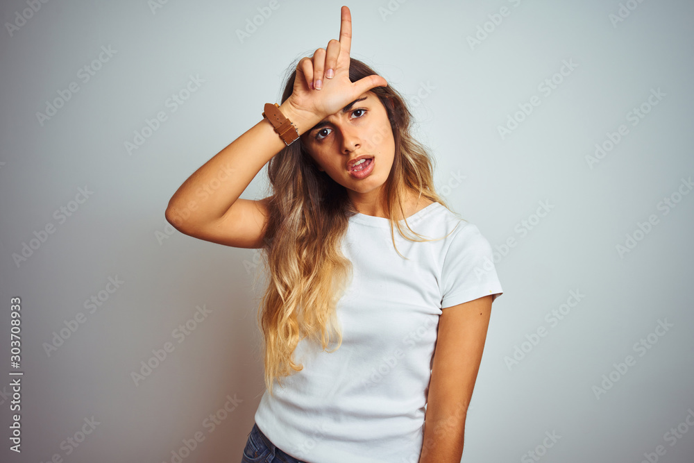 Canvas Prints Young beautiful woman wearing casual white t-shirt over isolated background making fun of people with fingers on forehead doing loser gesture mocking and insulting.