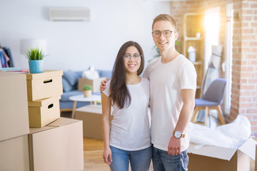 Fototapeta na wymiar Young beautiful couple wearing glasses standing at new home around cardboard boxes
