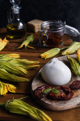 burrata cheese, dried tomatoes, zucchini flowers, olive oil on rustic wooden table