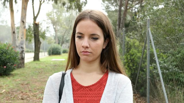 Front view portrait of a single sad woman walking alone in a park