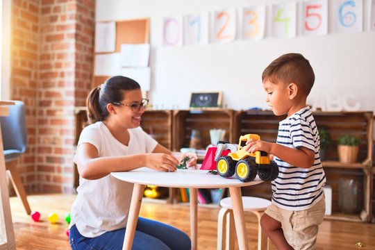 Beautiful teacher and toddler boy playing with tractor and cars at kindergarten