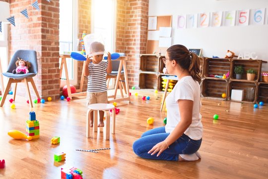 Beautiful teacher and toddler boy playing with plastic basket at kindergarten