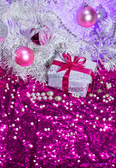 White fir branches with pearls, balls and gift box on the shining pink sequin background. New year celebration, party and fashion concept.