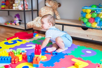 Beautiful toddler sitting on puzzle carpet playing with building blocks at kindergarten