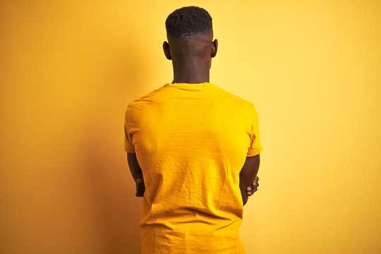 Young african american man wearing casual t-shirt standing over isolated yellow background standing backwards looking away with crossed arms