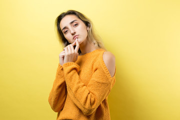 Portrait of a beautiful girl in an orange sweater, looks aside with pensive expression, is considering a plan for further action.	