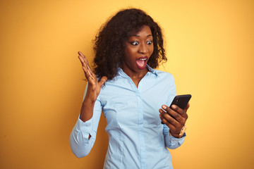 Naklejka premium Young african american woman using smartphone standing over isolated yellow background very happy and excited, winner expression celebrating victory screaming with big smile and raised hands