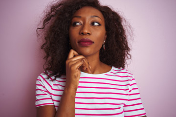 Fototapeta na wymiar Young african american woman wearing striped t-shirt standing over isolated pink background with hand on chin thinking about question, pensive expression. Smiling with thoughtful face. Doubt concept.