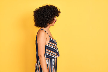 Arab woman with curly hair wearing striped colorful dress over isolated yellow background looking...