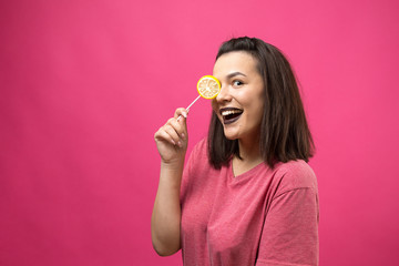 Portrait of lovely sweet beautiful cheerful woman with straight brown hair holding a lollipop near the eyes.	