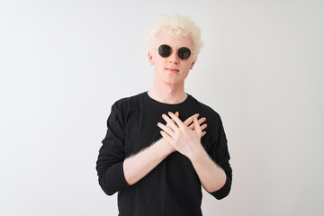 Young albino man wearing black t-shirt and sunglasess standing over isolated white background smiling with hands on chest with closed eyes and grateful gesture on face. Health concept.