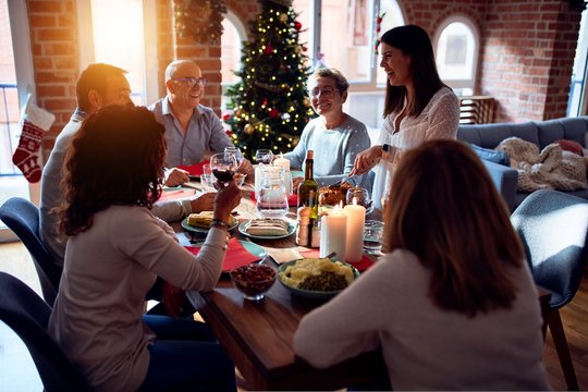 Family And Friends Dining At Home Celebrating Christmas Eve With Traditional Food And Decoration, Preparing Turkey For Dinner