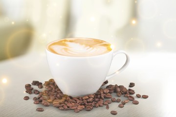 a Cup of coffee with cream and coffee beans on the table in the glare