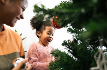 Mother and daughter african american girl decorating Christmas tree with ,arranging the christmas...