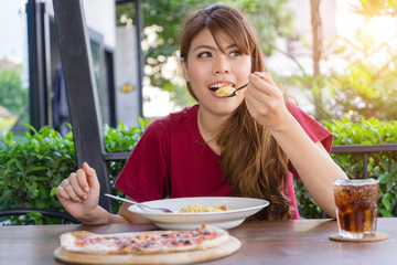 Young woman eating pasta, Spaghetti and pizza with soft drink on table in restaurant outdoor. Happy eating traditional Italian food, lifestyle concept. Hungry Asian girl having food alone.