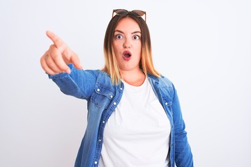Beautiful woman wearing denim shirt standing over isolated white background Pointing with finger surprised ahead, open mouth amazed expression, something on the front