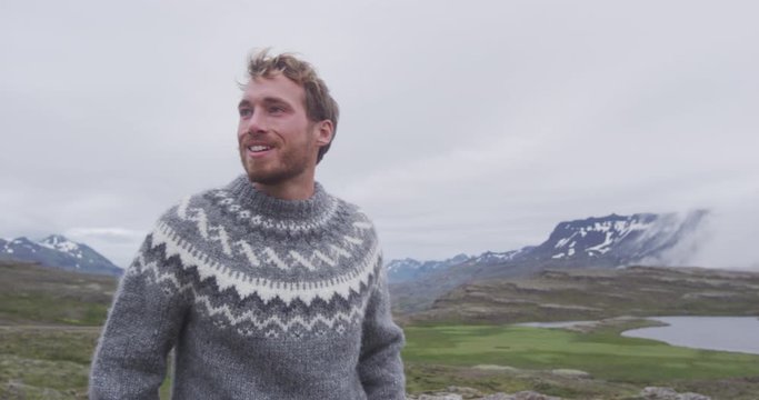 Portrait of man in Icelandic sweater outdoor smiling walking in nature on Iceland. Portrait of good looking bearded male model in nature wearing typical wool clothing.