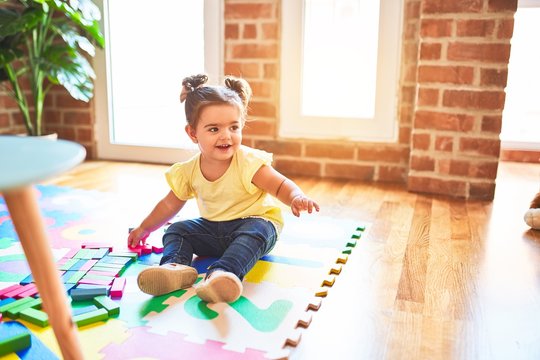Beautiful toddler sitting on puzzle carpet playing with wooden building blocks smiling at kindergarten