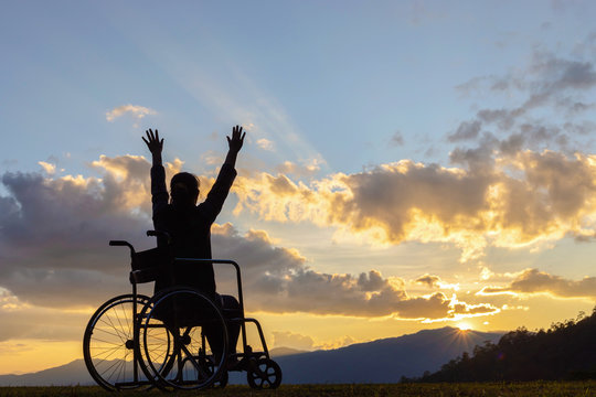 Happy disabled woman in a wheelchair and stretching hands at sunset. back view,