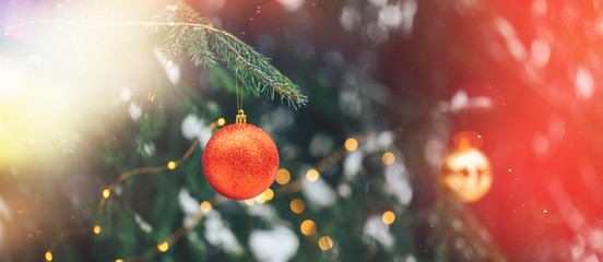Red christmas ball hanging on branch on sruce tree outdoor, snow, winter, with decorations.