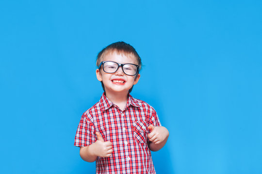 Funny Little Boy In Glasses Show Thumb And Happy Smile In Red Shirt On Blue Background.