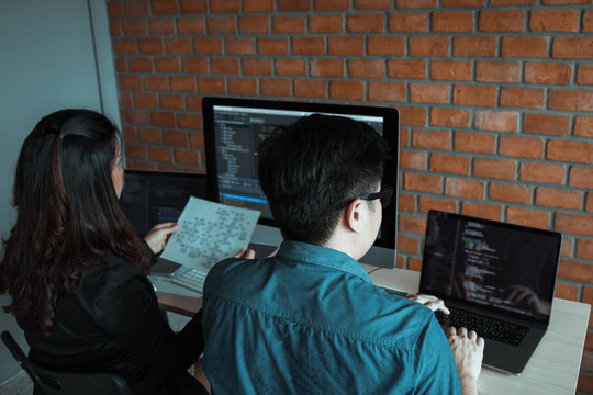 Two software developers are using computers to work together with their partner at the office desk.