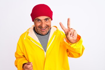 Fototapeta na wymiar Middle age man wearing rain coat and woolen hat standing over isolated white background showing and pointing up with fingers number two while smiling confident and happy.