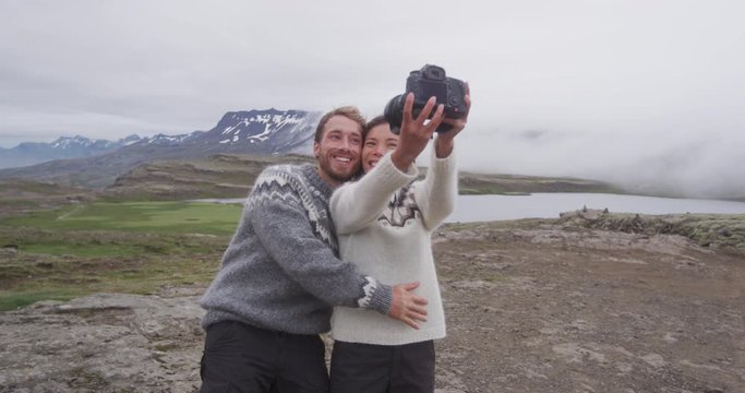 Iceland couple selfie wearing Icelandic sweaters in beautiful nature landscape on Iceland with camera. Woman and man model in typical Icelandic sweater. Multiracial couple, Asian woman, Caucasian man.
