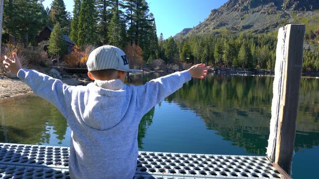 Child stretching out his arms as he looks out into a beautiful lake scenery. 4K conceptual stock footage video.