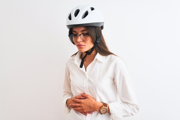Beautiful businesswoman wearing glasses and bike helmet over isolated white background with hand on stomach because nausea, painful disease feeling unwell. Ache concept.