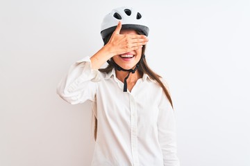 Beautiful businesswoman wearing glasses and bike helmet over isolated white background smiling and laughing with hand on face covering eyes for surprise. Blind concept.