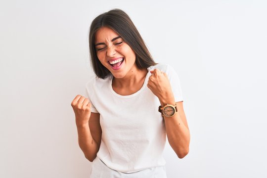Young beautiful woman wearing casual t-shirt standing over isolated white background very happy and excited doing winner gesture with arms raised, smiling and screaming for success. 