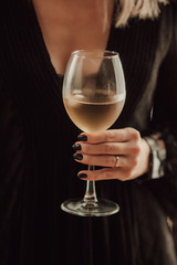  female hand, black manicure, in a black dress with a neckline hold a cold wet glass of white wine