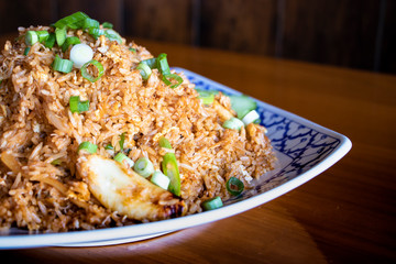 Close up of crab fried rice on top with green spring onion - ingredient of jasmine rice, crab, egg and seasoning sauce. Thai style. Serve on ceramic plate on wood table.