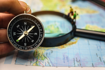 A compass that is used to travel with a magnifying glass and map that has a blurry background.