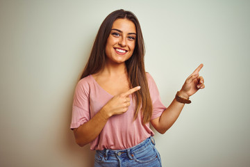 Young beautiful woman wearing casual t-shirt standing over isolated white background smiling and looking at the camera pointing with two hands and fingers to the side.