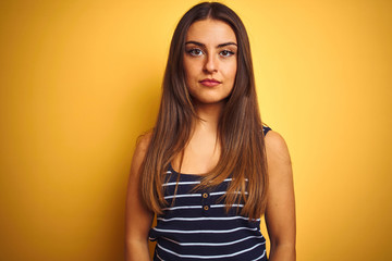 Obraz premium Young beautiful woman wearing striped t-shirt standing over isolated yellow background with serious expression on face. Simple and natural looking at the camera.