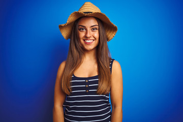 Young beautiful woman wearing striped t-shirt and summer hat over isolated blue background with a happy and cool smile on face. Lucky person.