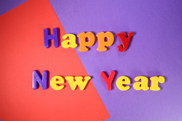 Plastic alphabet sign lettering Happy New Year on purple violet orange red paper background
