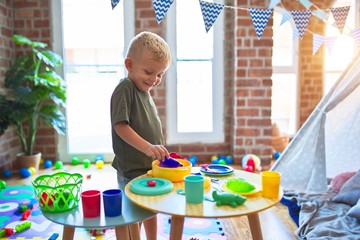 Young caucasian kid playing at kindergarten with toys. Preschooler boy happy at playroom.