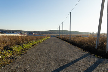 Dirt road with electric poles in a cottage village. Autumn, sunny