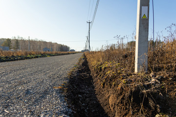 Dirt road with ditch and electric poles in a cottage village. Autumn, sunny