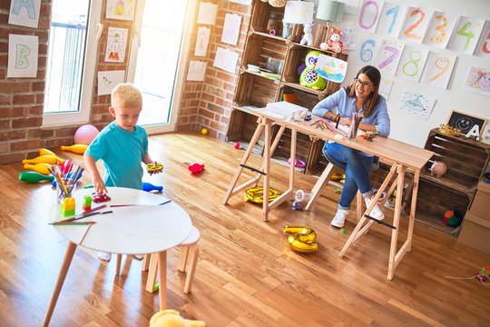 Young caucasian child playing at playschool with teacher. Young woman sitting on the desk of the classroom
