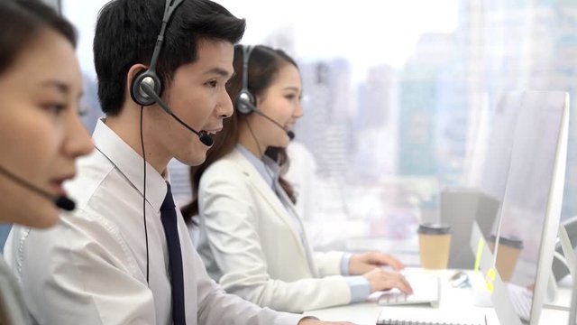 Handsome Asian male telemarketing operator working with team at call center city office