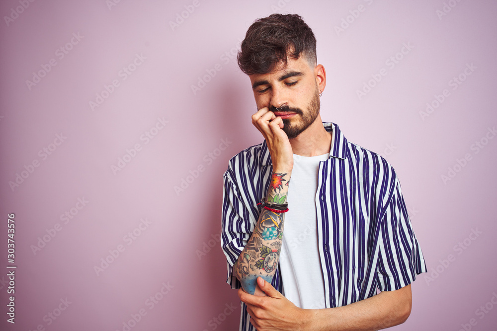 Wall mural Young man with tattoo wearing striped shirt standing over isolated pink background thinking looking tired and bored with depression problems with crossed arms. - Wall murals