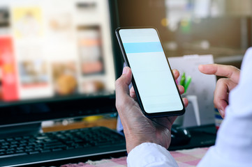 Cropped shot of man using smartphone while working at office desk, blank screen for graphic design.